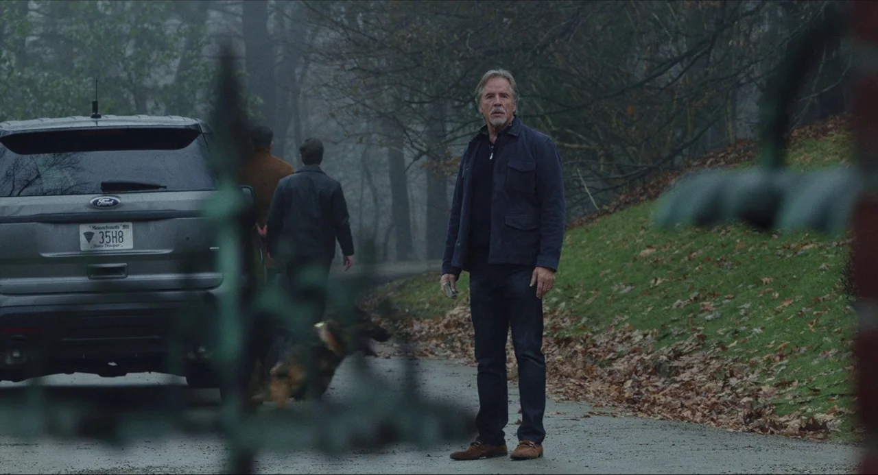 Knives Out (2019) movie still: fullbody — A wet asphalt driveway is lined by a wooded area with bare trees. A man stands near a grey SUV while other…