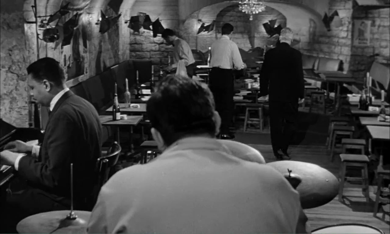 Paris Blues (1961) movie still: medium — A stone-walled basement nightclub featuring dark booths and tables under arched ceilings. A drummer plays…