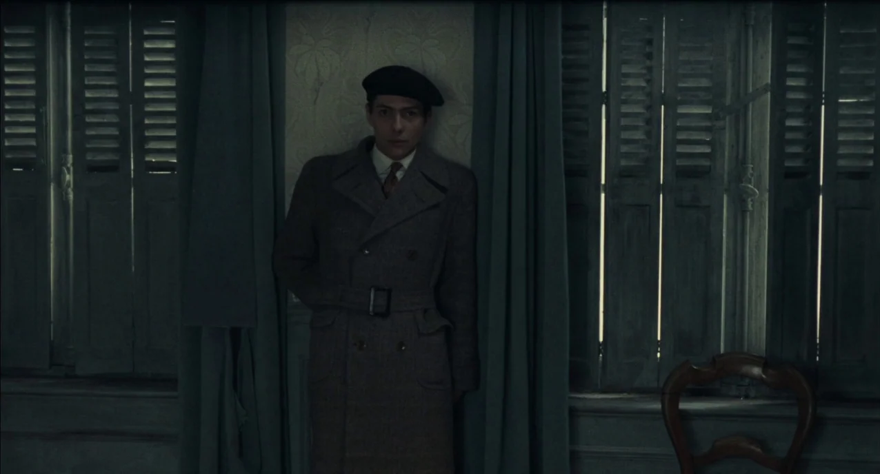The Army of Shadows (1969) movie still: medium — A dimly lit room features walls with faded wallpaper and closed wooden shutters. A young man in a…