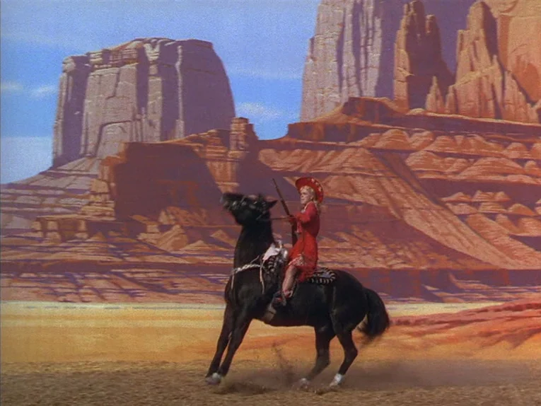Annie Get Your Gun (1950) movie still: wide — A woman rides a black horse in front of a painted backdrop of Monument Valley. The desert floor is…