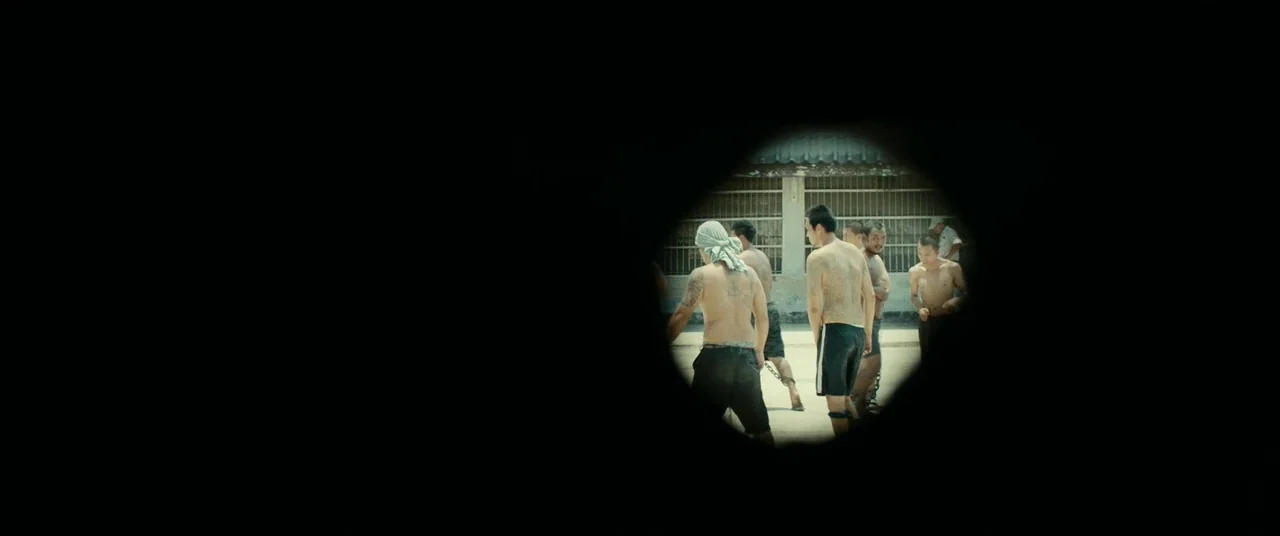 A Prayer Before Dawn (2017) movie still: wide — A group of shirtless men with tattoos stand in a walled outdoor area. They appear to be in a secure…