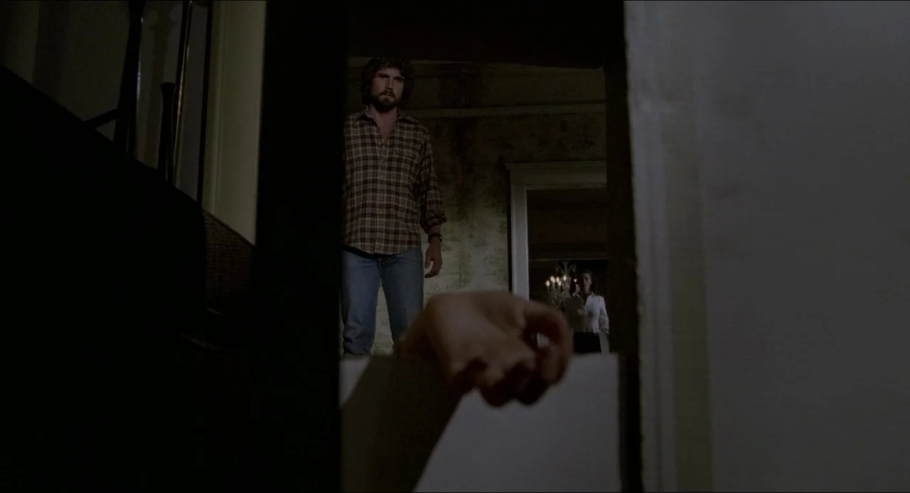 The Amityville Horror (1979) movie still: medium — An dimly lit interior hallway with textured wallpaper showing faint signs of age and wear. A man…