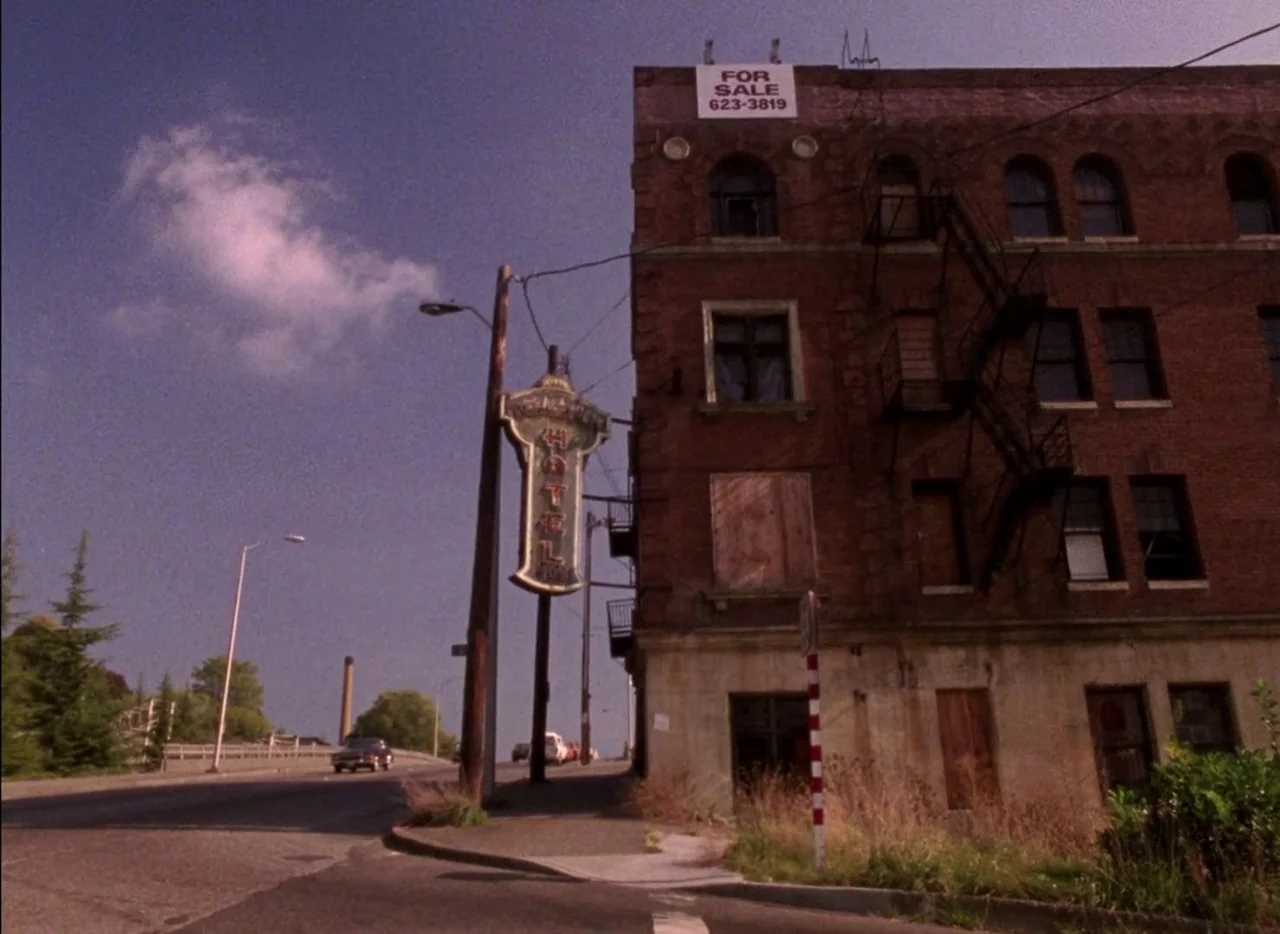 Streetwise (1984) movie still: establishing — A multistory brick hotel building features boarded windows and a prominent hotel sign. A for-sale sign…