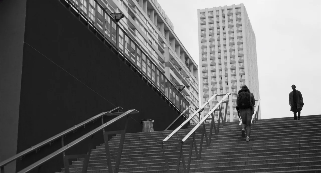 Paris, 13th District (2021) movie still: wide — A wide outdoor concrete staircase leads upward toward modern multi-story residential apartment…