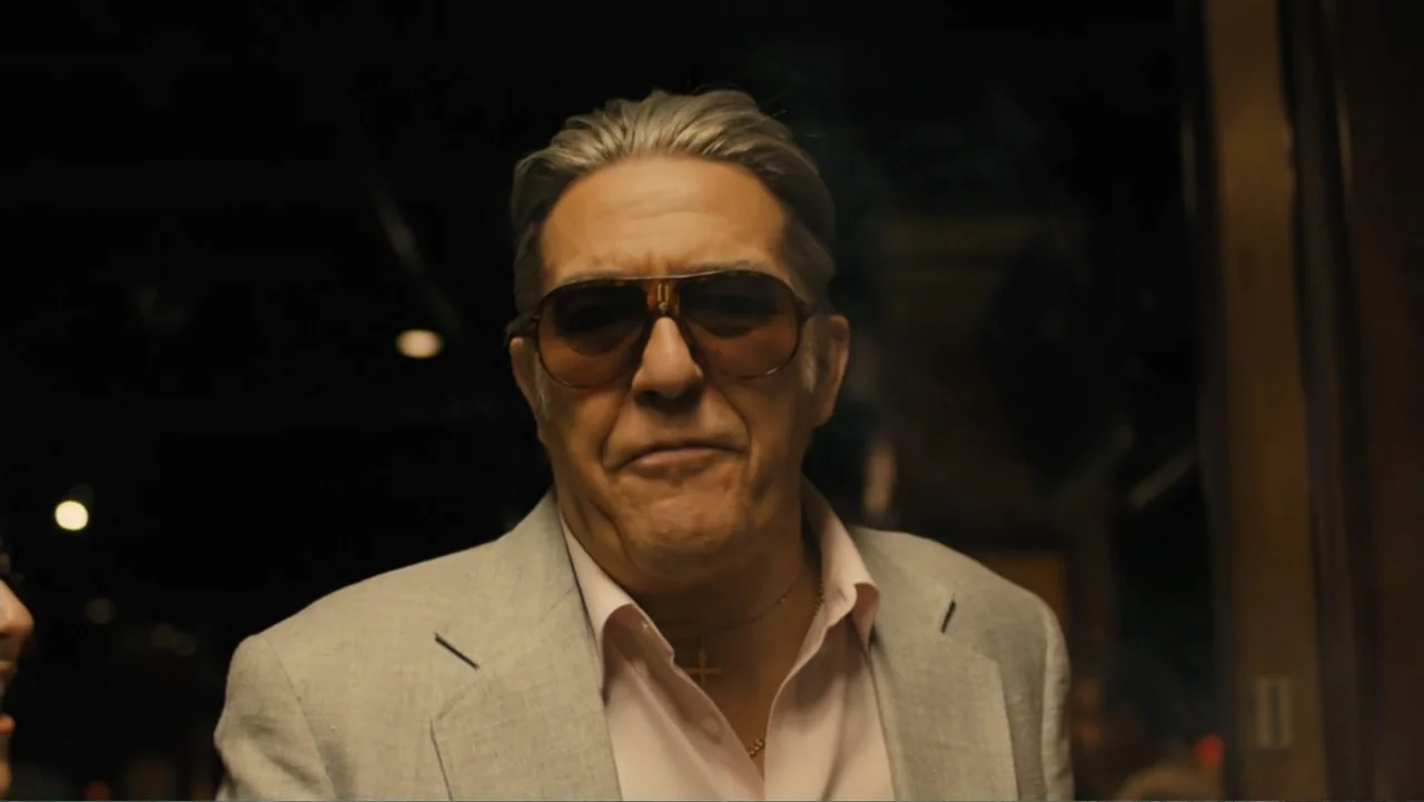 Bleed for This (2016) movie still: medium — A dark, dimly lit environment features a man in a blazer and sunglasses. The man faces the camera…