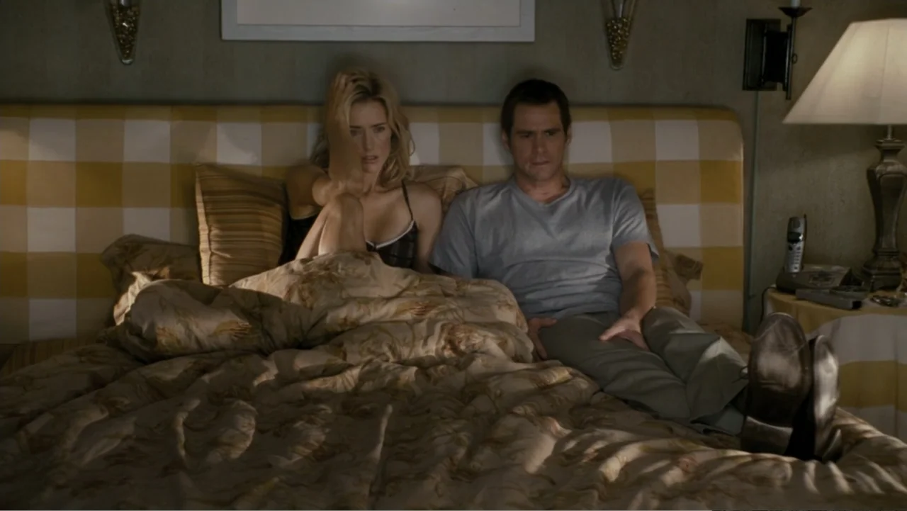 Fun with Dick and Jane (2005) movie still: medium — A modern hotel bedroom features a large bed with a yellow and white checkered headboard. A man…