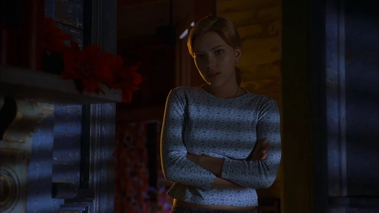 Love Song For Bobby Long (2004) movie still: medium — A dimly lit interior room at night features a doorway and wooden siding. A young woman stands…