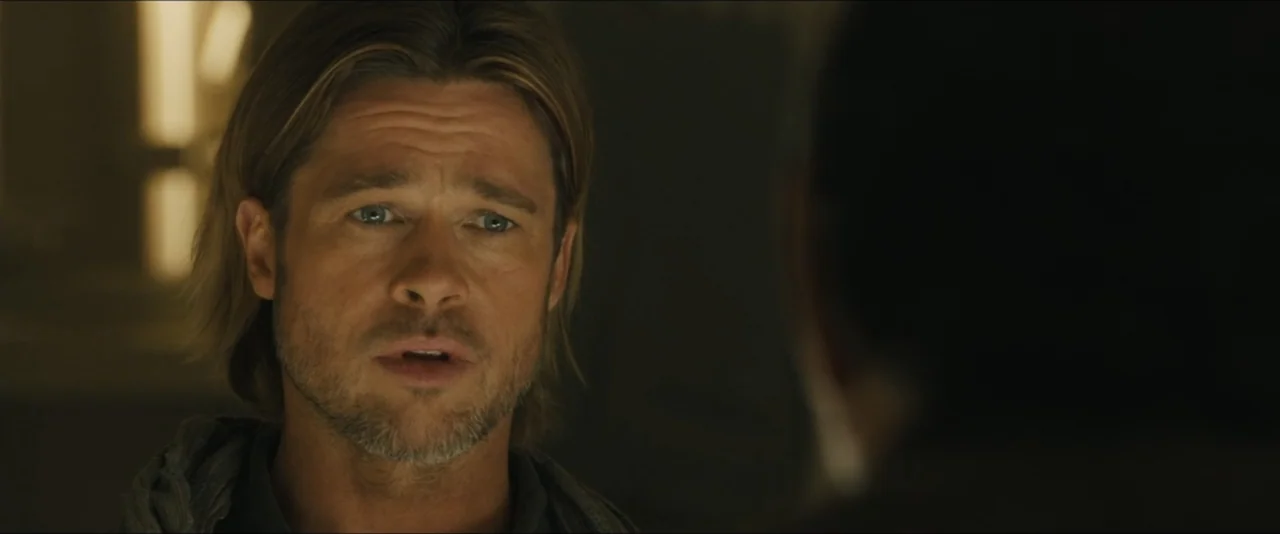 World War Z (2013) movie still: closeup — A dimly lit indoor space with blurred background details visible in the soft focus. A man with…