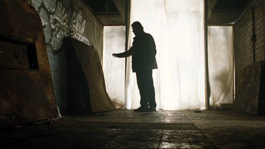 We Are The Night (2010) movie still: fullbody — An abandoned industrial room with white brick walls covered in faint graffiti and grime. A man…