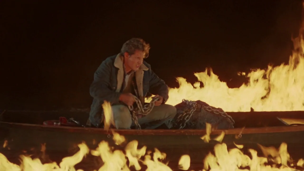 Friday the 13th Part VI: Jason Lives (1986) movie still: medium — A man sits in a small wooden boat surrounded by rising flames at night. He stares…