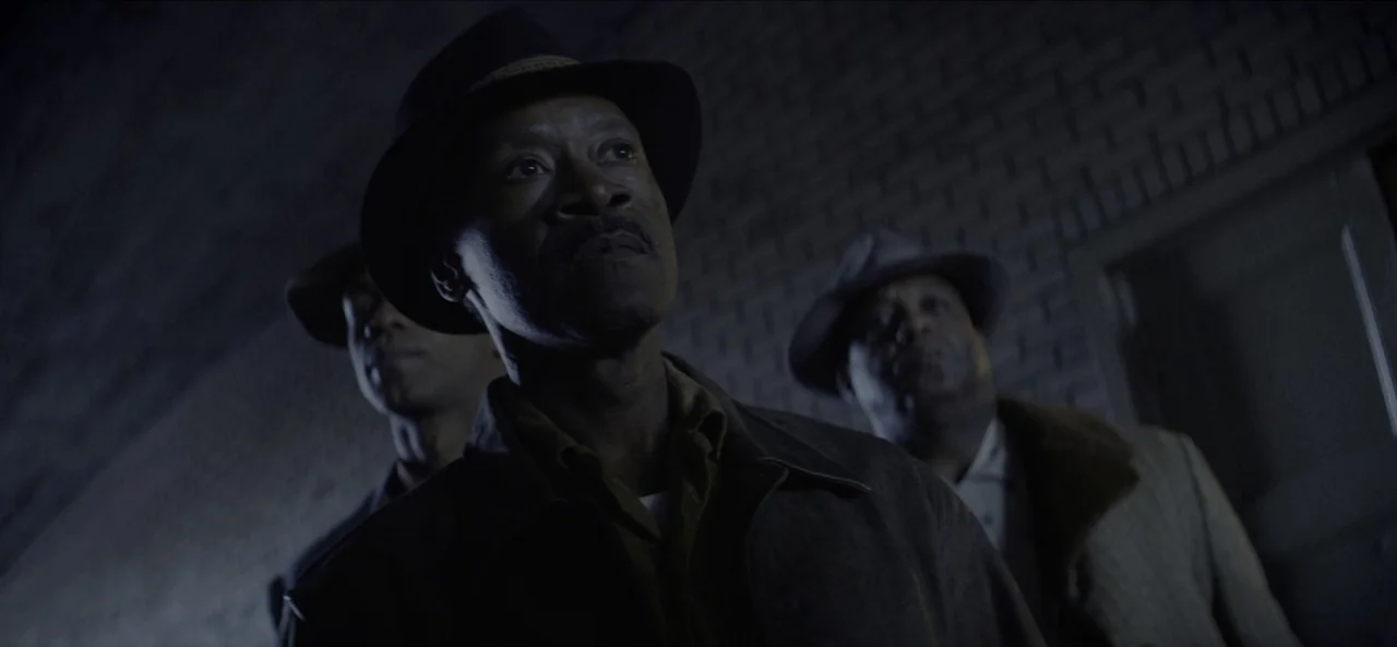 No Sudden Move (2021) movie still: medium — Three men stand within a dark concrete underpass with a brick wall backdrop. The men wear fedoras and…