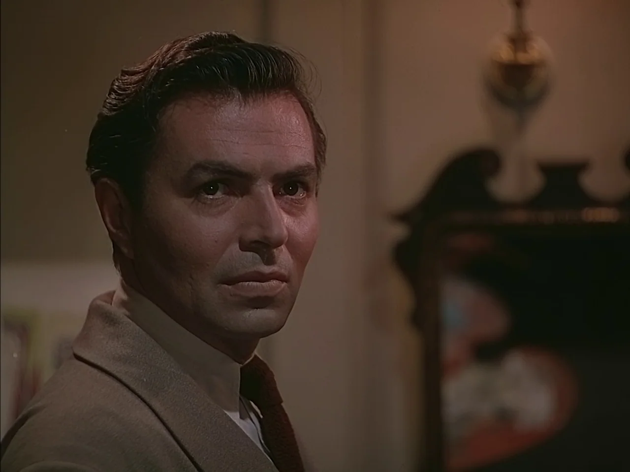 Pandora and the Flying Dutchman (1951) movie still: closeup — A man stands in a dimly lit indoor space with plain walls. He is captured in a…