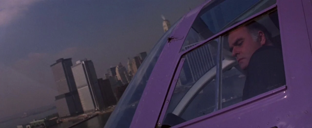 Klute (1971) movie still: medium — A view from inside a purple helicopter flying over the New York City waterfront. An older man sits in the pilot…