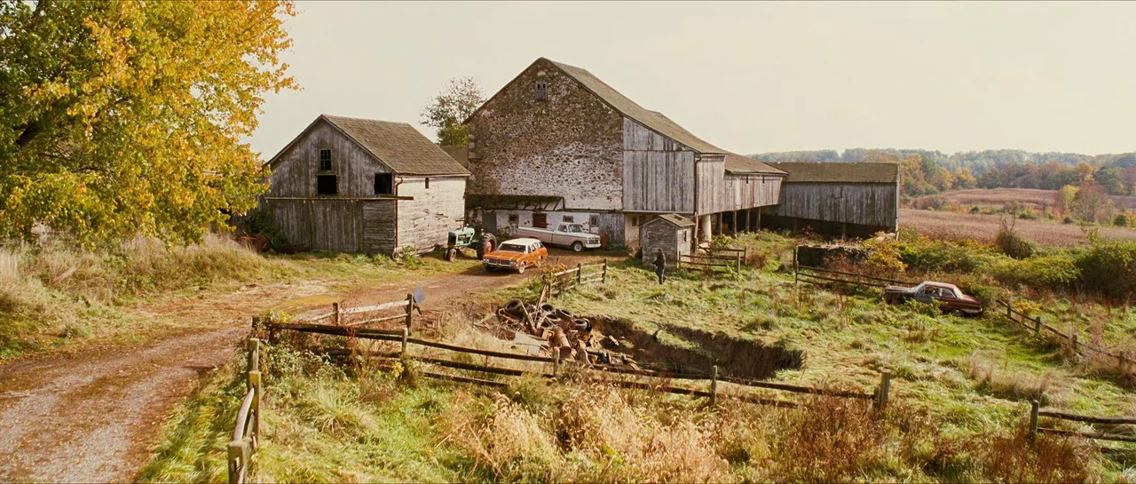 The Lovely Bones (2009) movie still: establishing — A rural farmstead features aged wooden barns and an old stone structure. Several vintage cars…