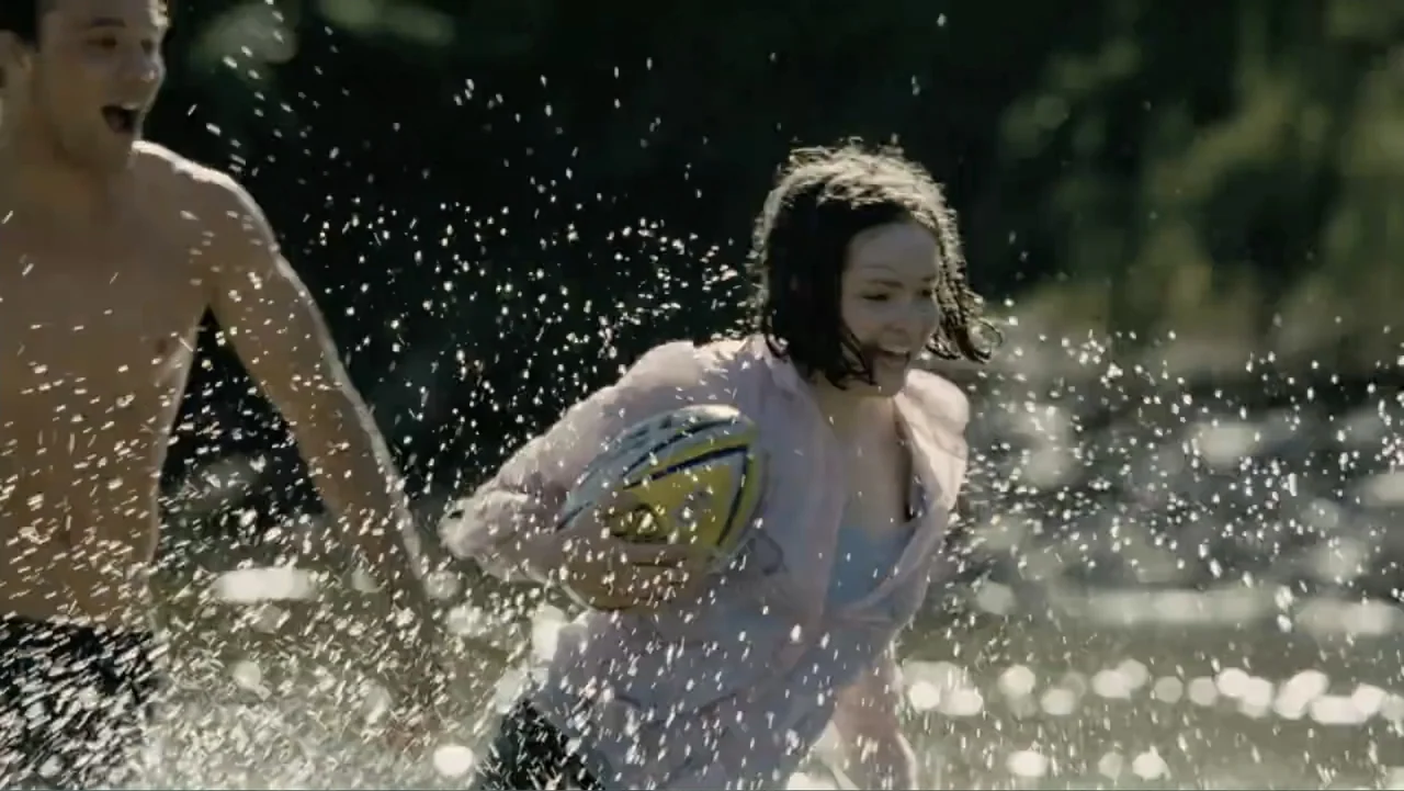 Tomorrow, When the War Began (2010) movie still: medium — A woman and a man run through shallow river water during the day. The woman carries a…