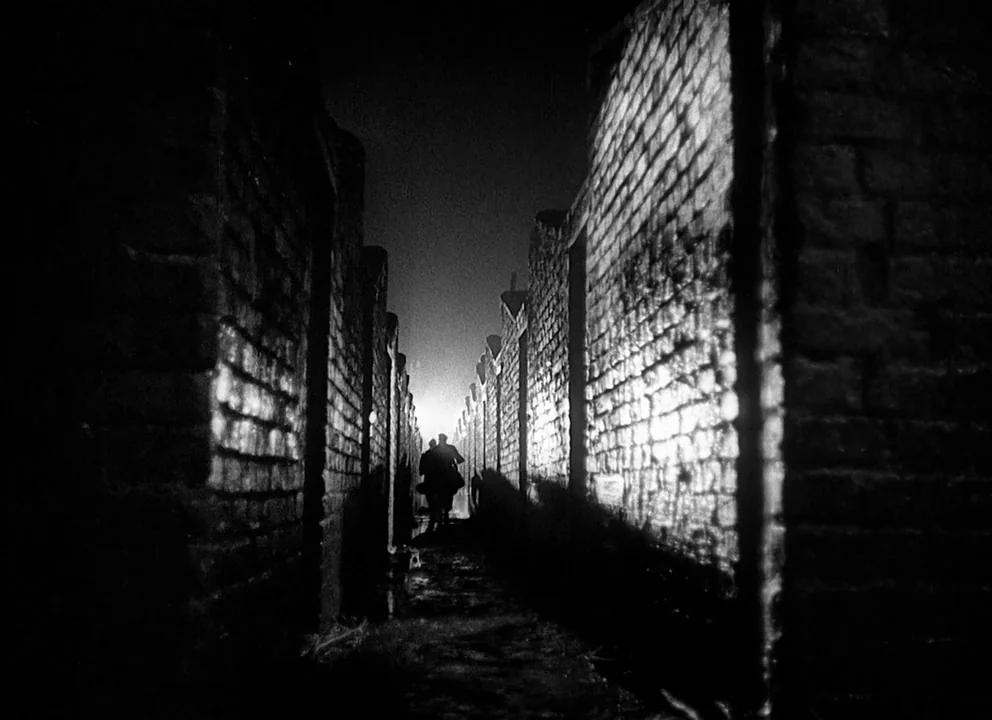 Odd Man Out (1947) movie still: wide — A narrow alleyway defined by high brick walls on either side in the dark. Two silhouettes walk away into the…