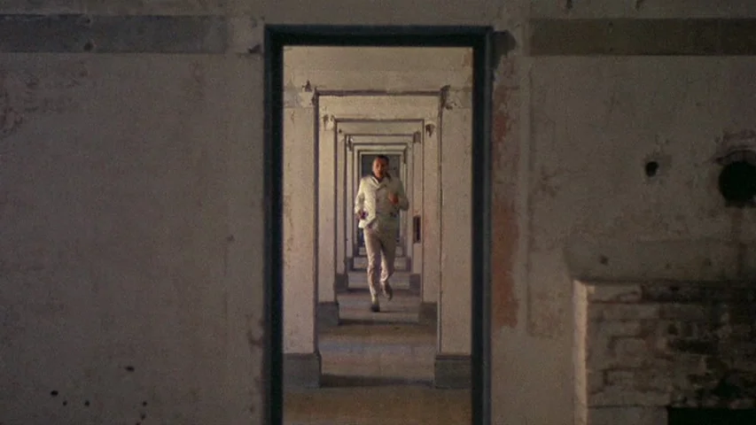 Petulia (1968) movie still: wide — An interior space features a series of aligned rectangular doorways creating a vanishing point. A man in a light…