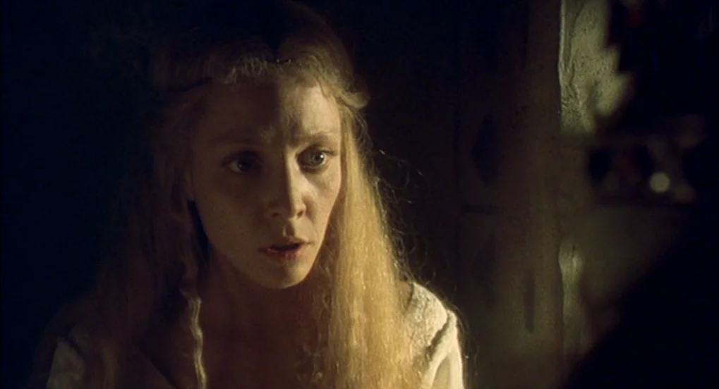 Jabberwocky (1977) movie still: closeup — A dimly lit stone chamber with rough textured walls creates a dark atmosphere. A young woman with long…
