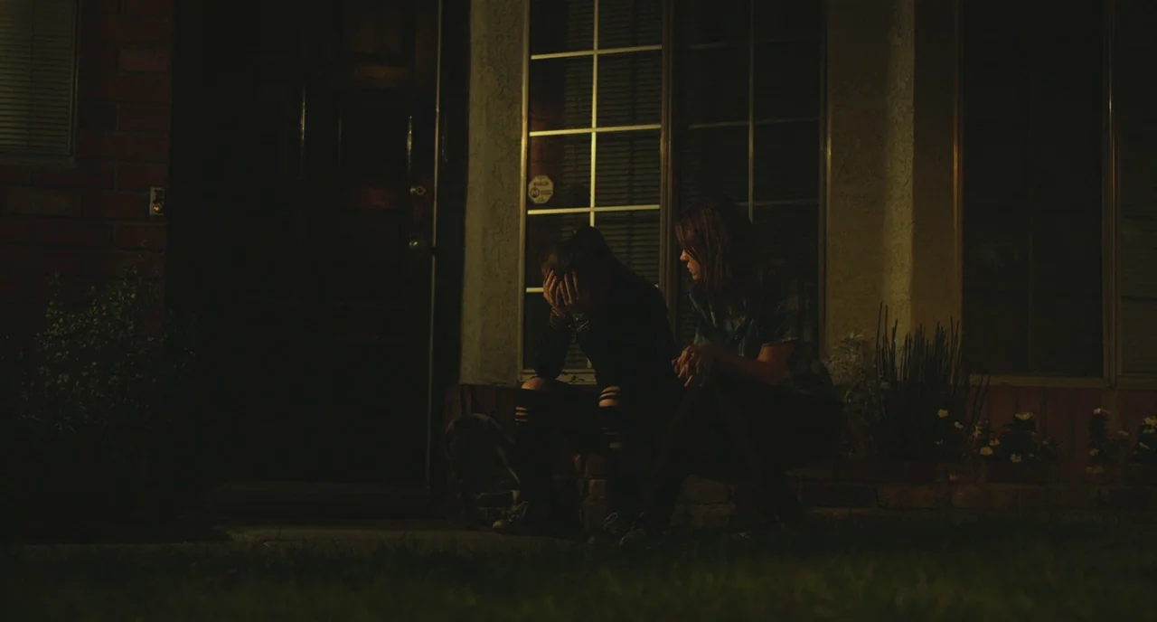Short Term 12 (2013) movie still: medium — A suburban house entrance at night with dark brick walls and a glass window. Two young women sit side by…