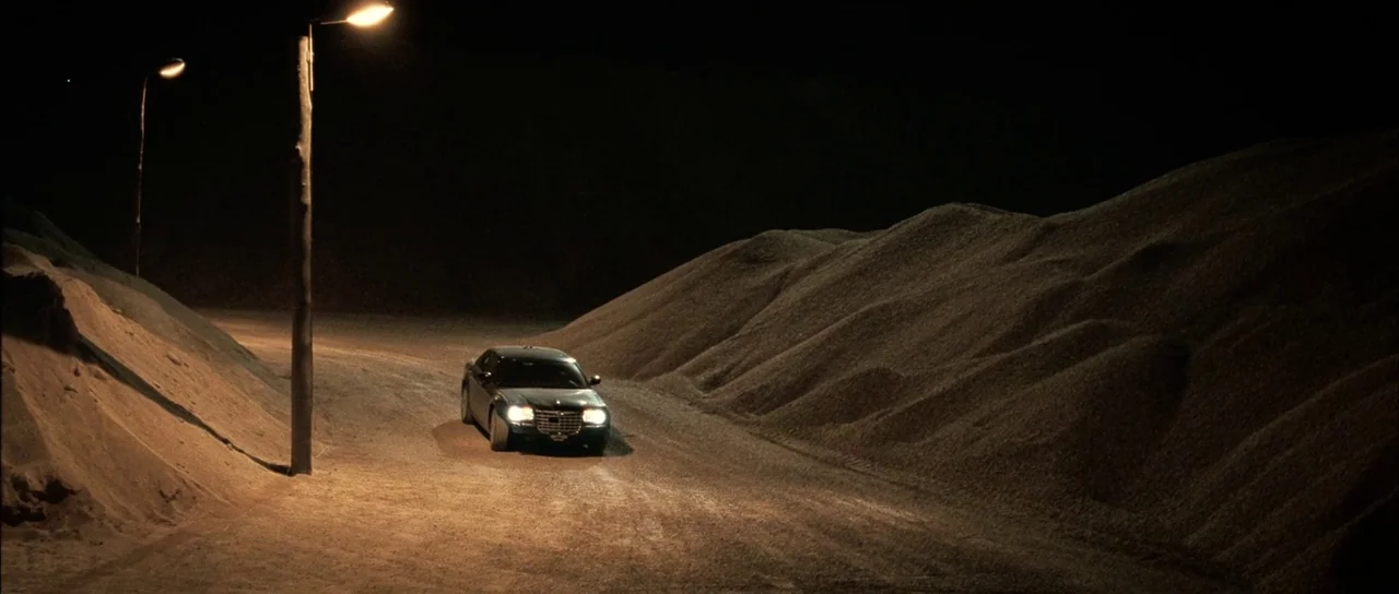 Daybreakers (2009) movie still: wide — A dark, desolate gravel quarry is enclosed by massive, looming piles of loose aggregate. A single black sedan…