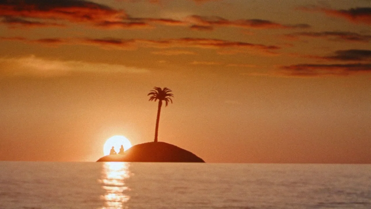 Strawberry Mansion (2021) movie still: wide — A tiny island with a single palm tree sits in the middle of the ocean. Two figures are seated on the…