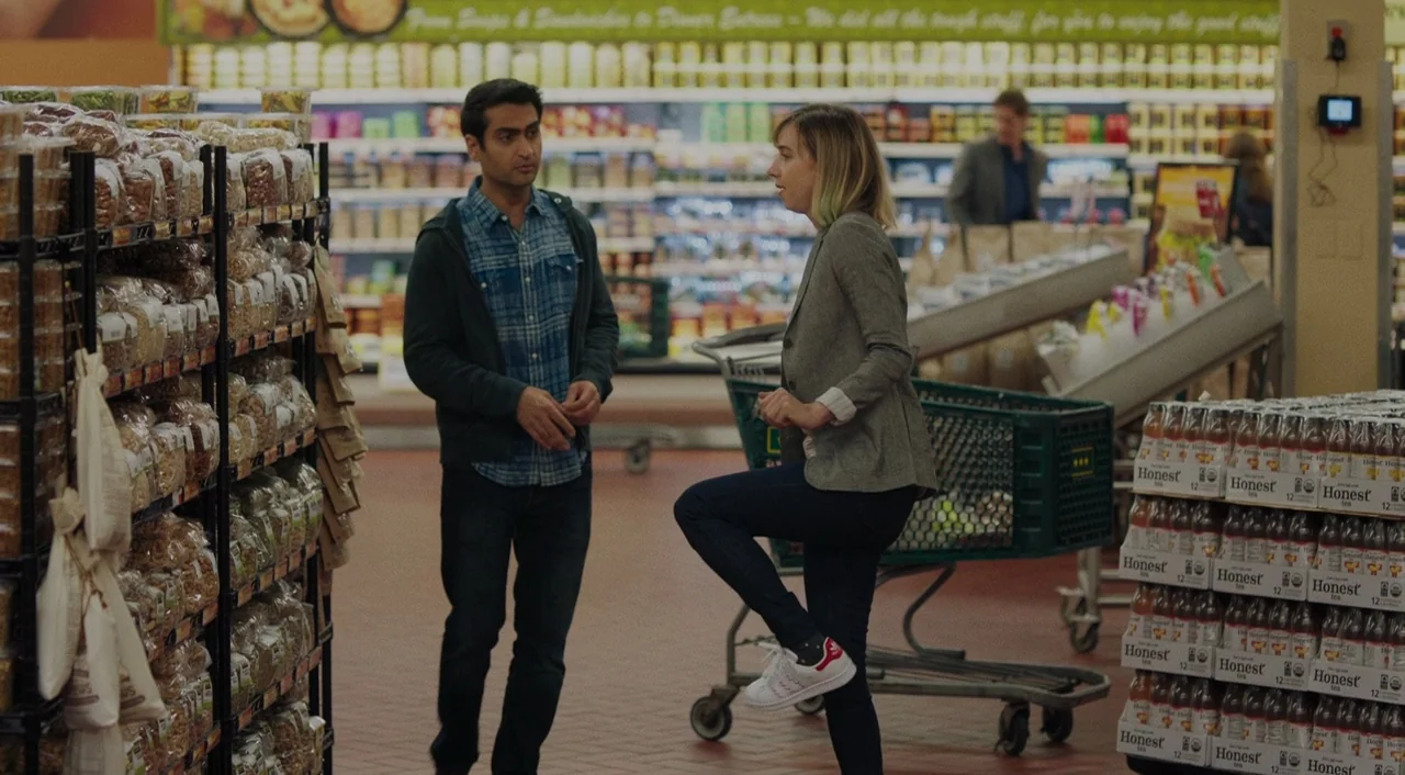 The Big Sick (2017) movie still: fullbody — A well-lit grocery store aisle contains stocked shelves of packaged goods and stacked beverages. A man…