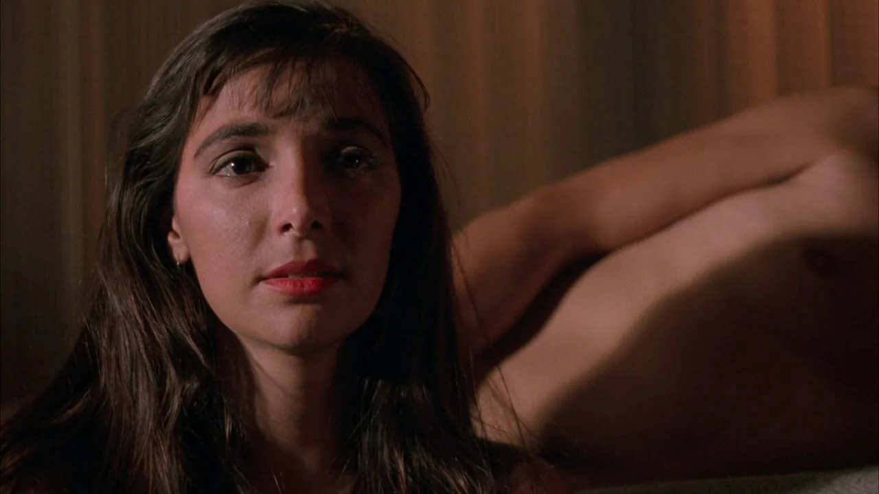 The Rapture (1991) movie still: closeup — A dimly lit room features a woman in the foreground and a man beside her. They are resting horizontally in…