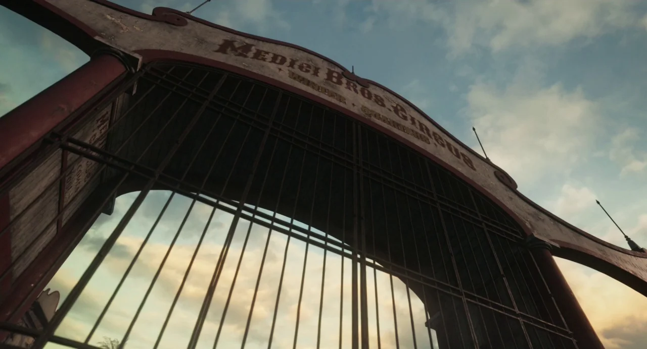 Dumbo (2019) movie still: establishing — A weathered iron and wooden archway marks the entrance to a circus grounds. The gate features faded red…