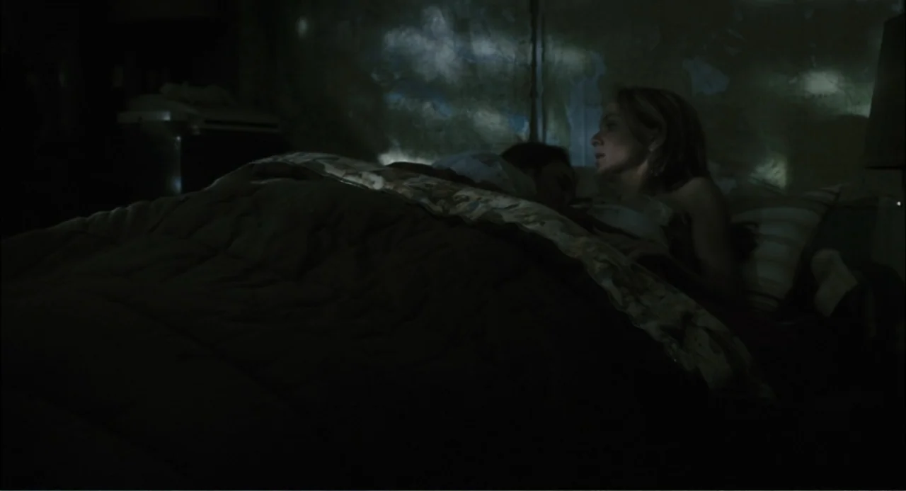El hijo del diablo (1966) movie still: medium — A dimly lit bedroom features a bed with a dark patterned comforter. A woman lies in bed beside…