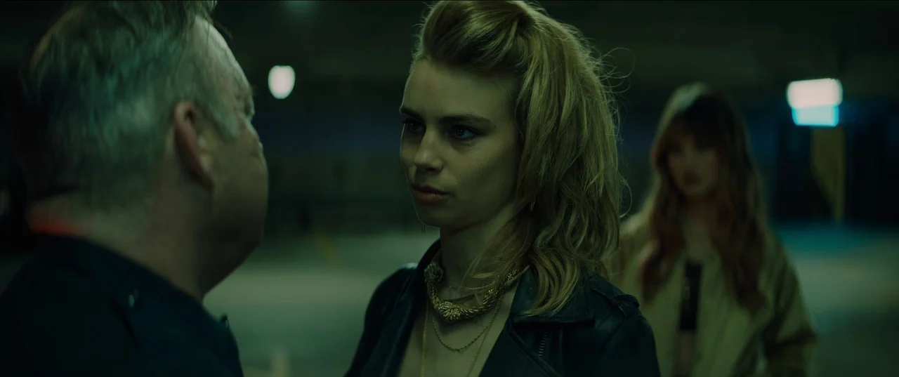 Night Teeth (2021) movie still: medium — A dark subterranean parking garage with visible overhead lighting fixtures in the background. A woman in a…