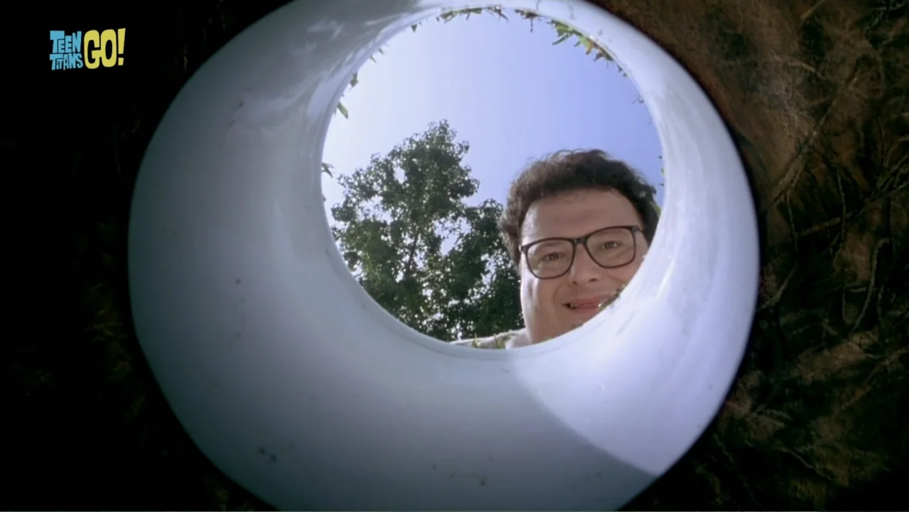 Teen Titans Go! To the Movies (2018) movie still: closeup — A man peers down into a cylindrical pipe embedded in the dark earth. He wears glasses…