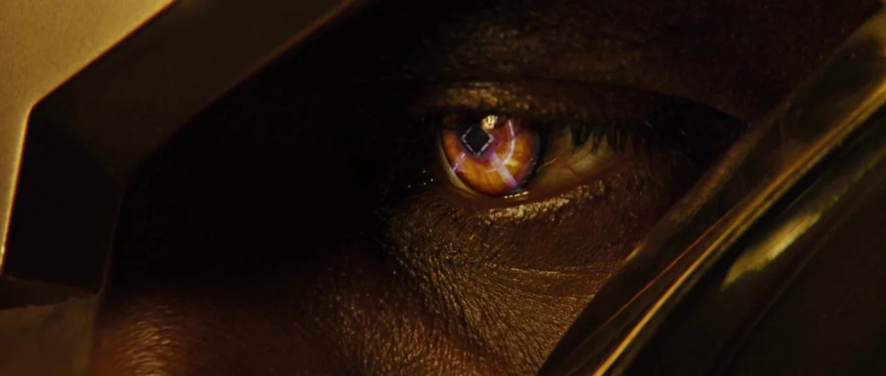 Thor (2011) movie still: closeup — A close-up of a human eye inside a dark metallic frame. The eye reflects a glowing orange and black screen…