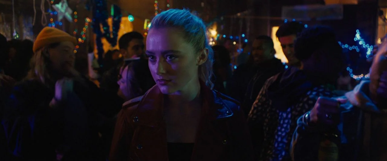 Freaky (2020) movie still: medium — A crowded, dimly lit indoor space is decorated with party lights and holiday streamers. A young woman with…
