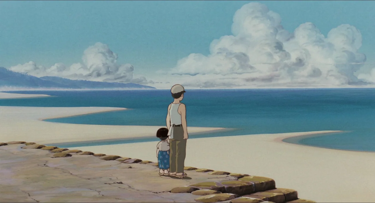Grave of the Fireflies (1988) movie still: fullbody — A stone seawall overlooks a calm, blue ocean under a vast, cloud-filled sky. A young boy in a…