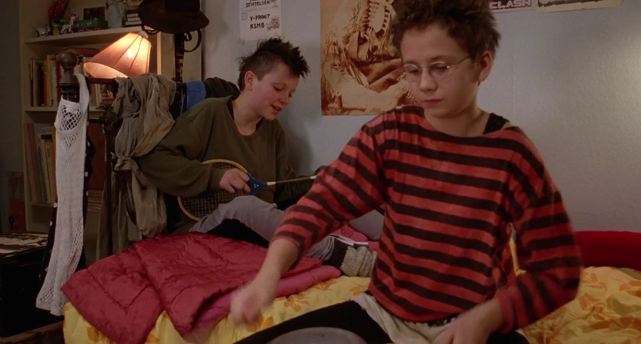 We Are The Best! (2013) movie still: medium — A cluttered teenager's room features a bed, a bookshelf, and posters on the wall. Two adolescents sit…
