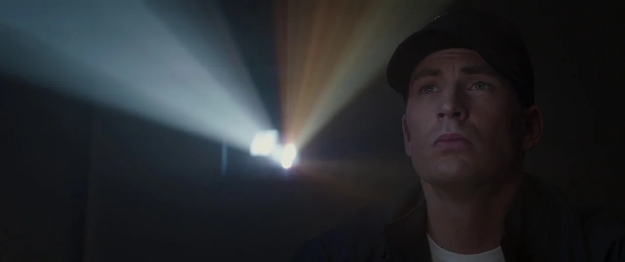 Captain America: The Winter Soldier (2014) movie still: closeup — A dark movie theater interior with a visible beam of light from a projector. A man…