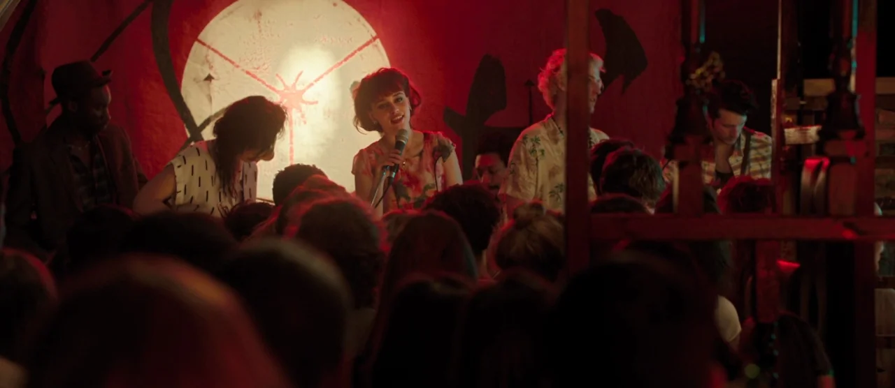 Dom Hemingway (2013) movie still: medium — A dimly lit stage features a band performing in front of a painted red wall. A young woman with a short…
