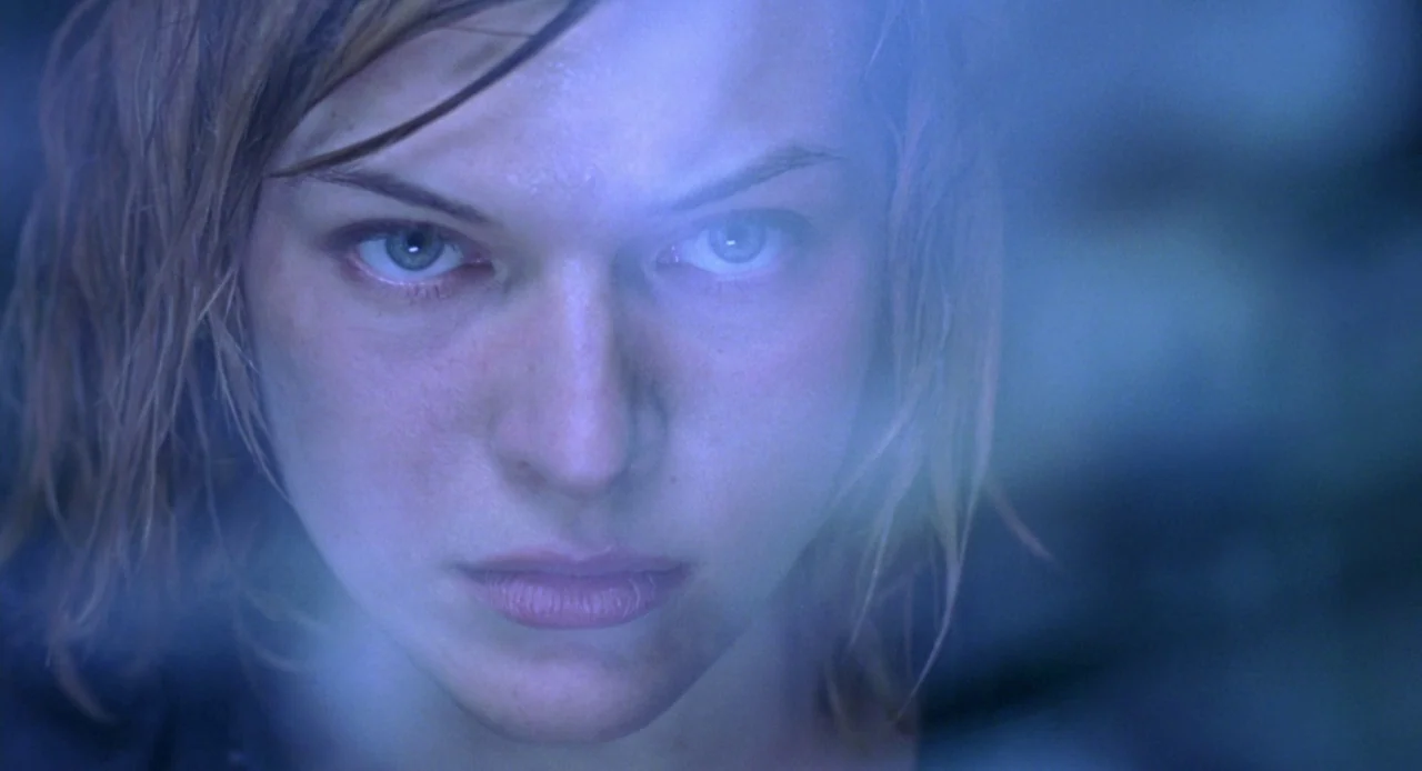 Resident Evil (2002) movie still: closeup — A close-up of a young woman behind a condensation-covered pane of glass. She stares directly into the…