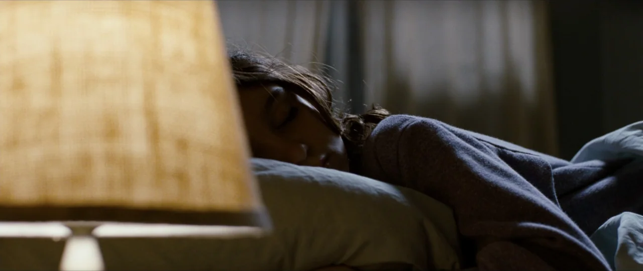 The Haunting in Connecticut (2009) movie still: closeup — A dimly lit bedroom features a sleeping woman in bed at night. The foreground is dominated…