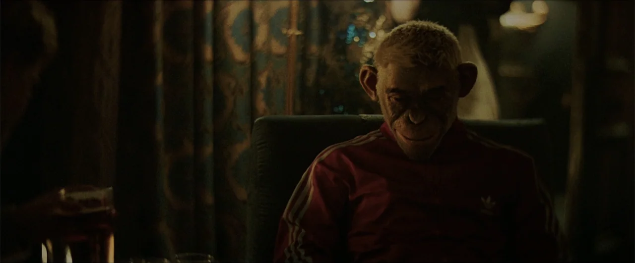 Better Man (2024) movie still: medium — A dark, dimly lit indoor setting features patterned curtains in the blurred background. An anthropomorphic…