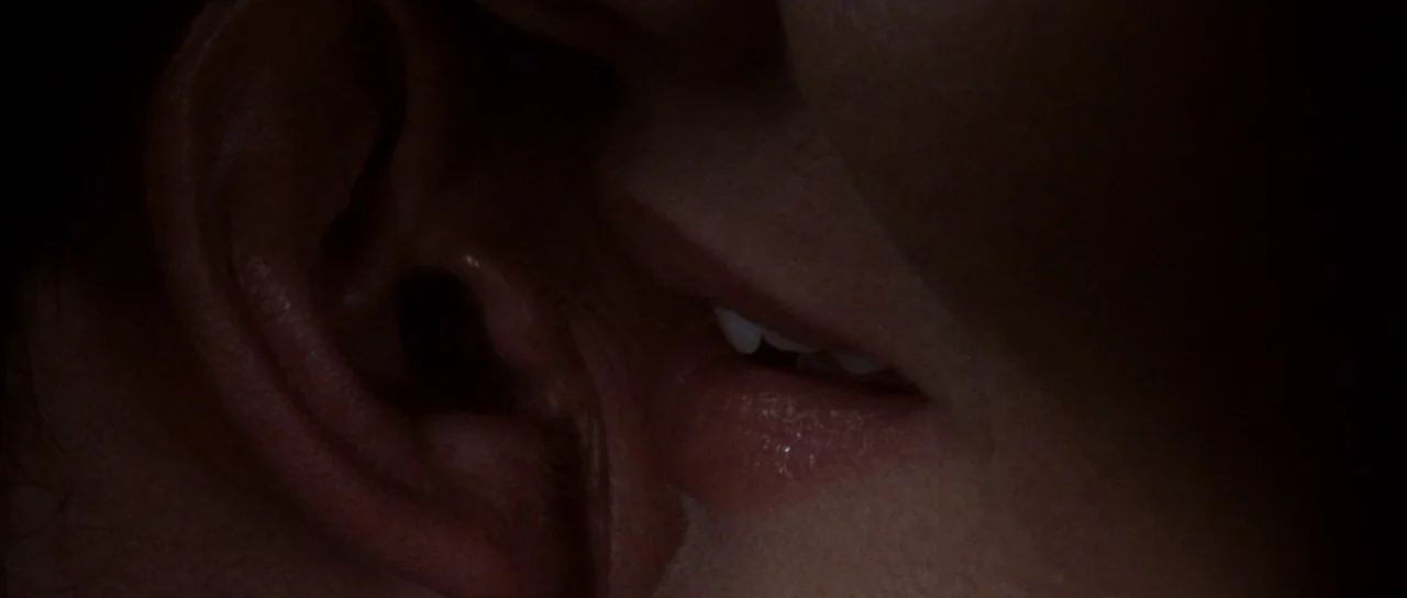 The Thomas Crown Affair (1999) movie still: closeup — A close-up view shows a person's mouth leaning against another person's ear. The background is…