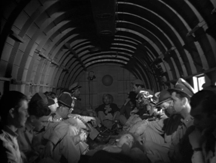 They Were Expendable (1945) movie still: wide — The interior of an airplane fuselage has curved ribbed metal walls and floor. A group of men in…