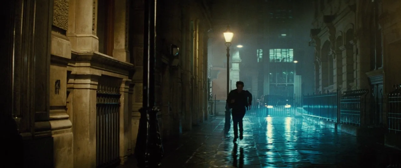 Mission: Impossible – Rogue Nation (2015) movie still: wide — A narrow stone-walled urban alleyway features wet pavement reflecting light from a…