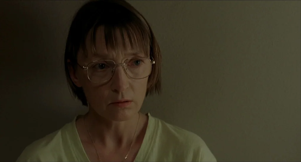 All or Nothing (2002) movie still: closeup — A woman stands in front of a plain, dull-colored interior wall. She is positioned slightly to the left…