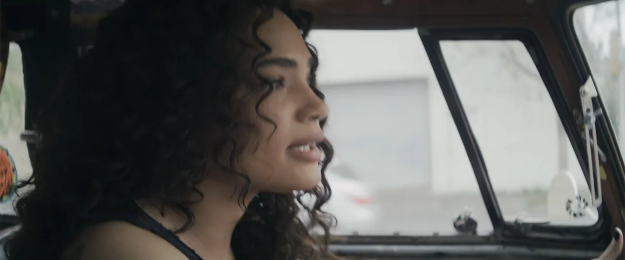 Holiday Harmony (2022) movie still: closeup — The interior of a vehicle features a dark dashboard and visible side windows. A woman with long curly…