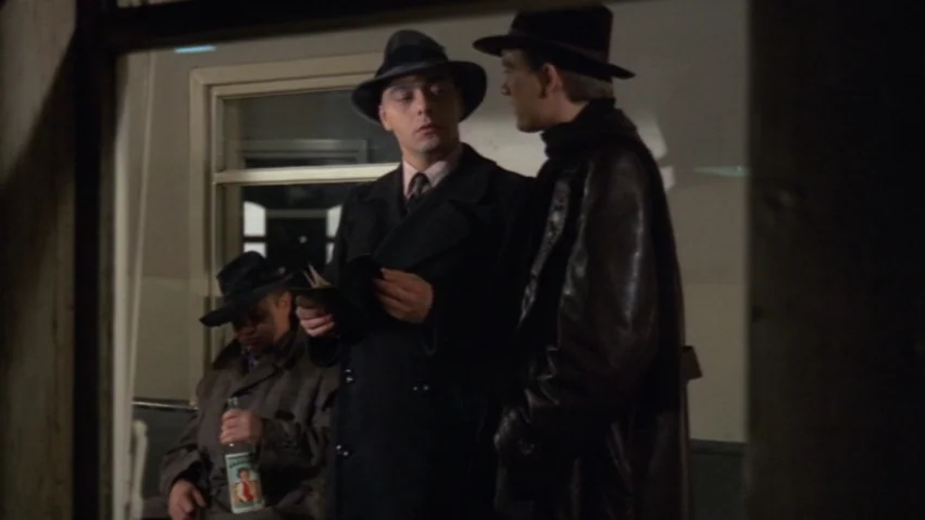Tenderness of the Wolves (1973) movie still: medium — A dimly lit passenger cabin with windows and a door in the background. Two men engage in…