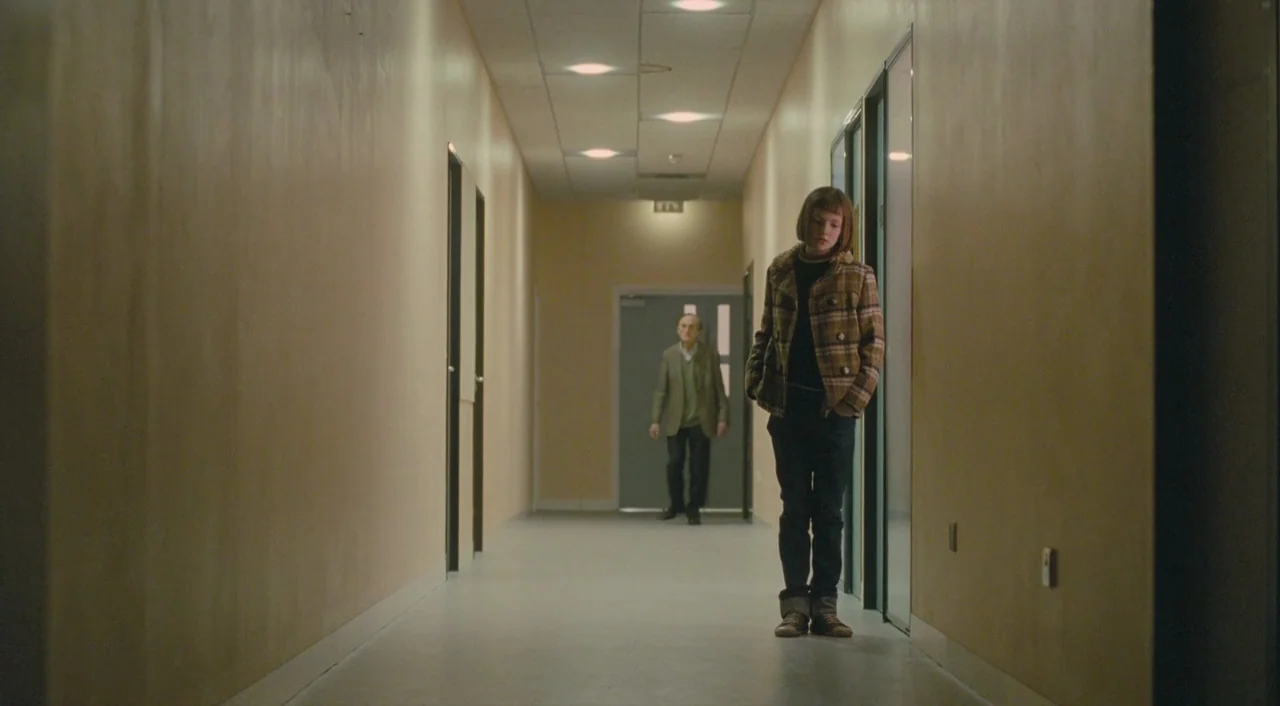 Broken (2012) movie still: fullbody — A long, brightly lit institutional corridor features yellow walls and white drop-ceiling tiles. A young girl…
