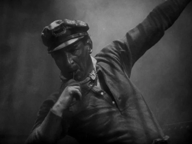The Docks of New York (1928) movie still: medium — A man stands on a metallic surface in an industrial environment filled with smoke. He keeps one…