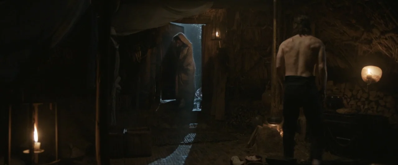 47 Ronin (2013) movie still: medium — A dark, earth-floored interior of a rustic hut features straw walls and simple lanterns. A shirtless man…