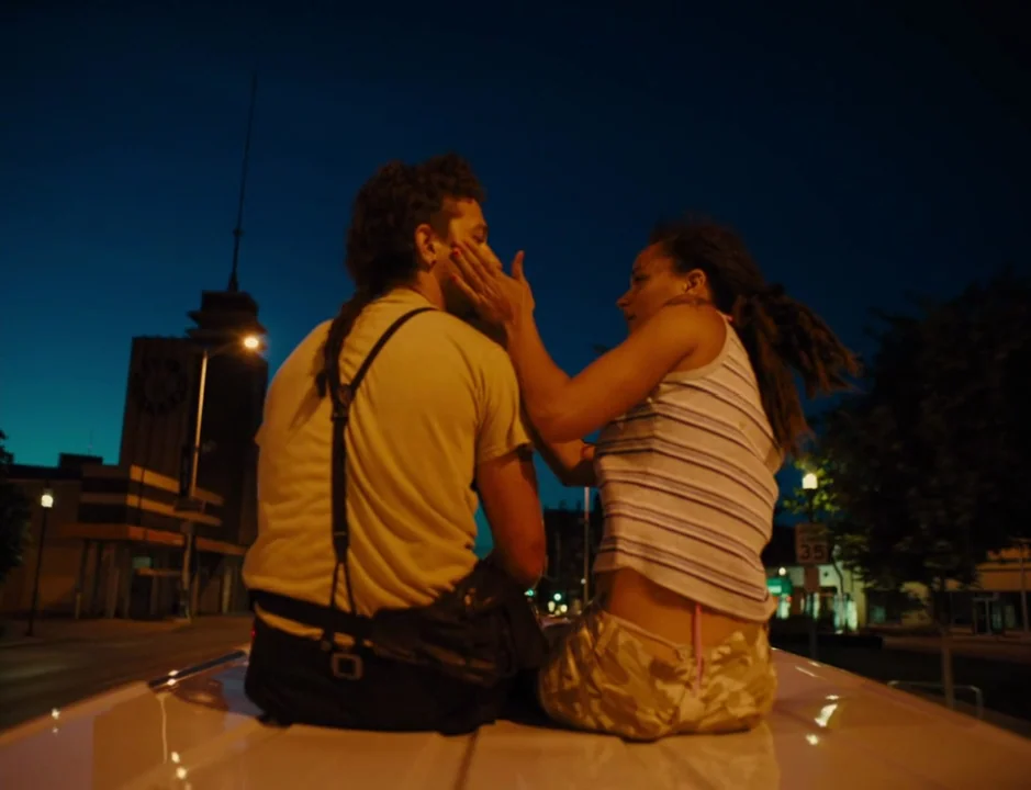 American Honey (2016) movie still: medium — A man and woman sit atop a vehicle at night under street lighting. The woman reaches out to touch the…